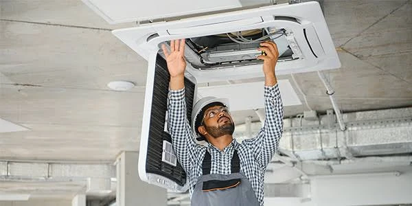 Technician working on a ceiling-mounted HVAC unit near overhead ducting